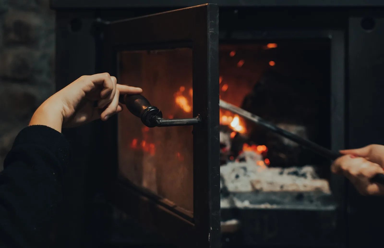 Main sur la poignée d'une porte de poêle à bois entrouverte devant le foyer en feu